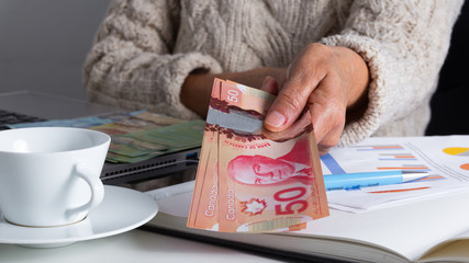 Banknotes of Canadian currency: Dollar. Old woman offering bills on table.
