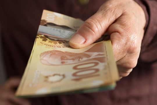 Banknotes of Canadian currency: Dollar. Front view senior person holding bills.