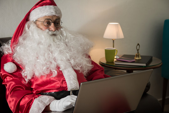 Sideways of Santa Claus relaxing in sofa at home Using laptop for communication and leisure or shopping online.