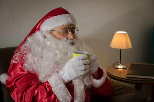 Sideways of Santa Claus relaxing in sofa at home enjoying a cup of coffee or tea.