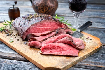 Fotobehang Traditional barbecue dry aged sliced roast beef steak with herbs as closeup on an old cutting board © HLPhoto