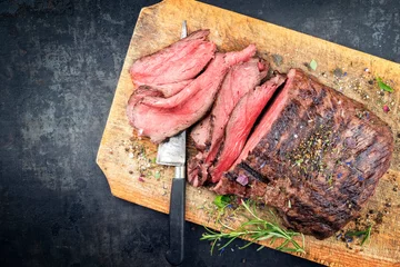 Foto auf Alu-Dibond Traditional barbecue dry aged sliced roast beef steak with herbs as top view on an old cutting board with copy space left © HLPhoto