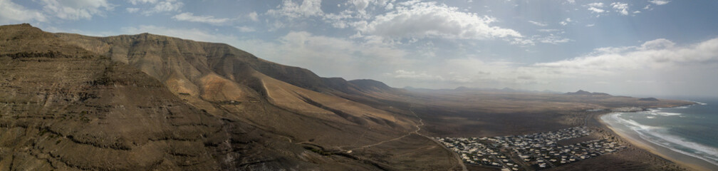 Vista aerea della spiaggia di Famara, Lanzarote, isole Canarie, Spagna. Risco di Famara, rilievo, montagne a picco sull’Oceano Atlantico. Strada non asfaltata che costeggia la costa