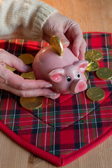 Female hand holds Piggy bank for luck on the background of chocolate coins and wooden table with the serving napkin.Low angel view.Tonned image