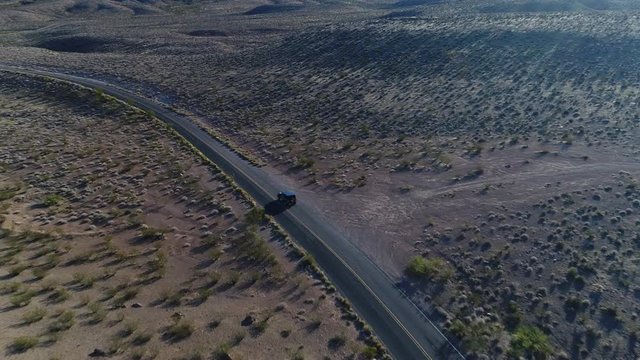 An incredible aerial reveal of a car taking a curve in a vast valley between imposing mountains