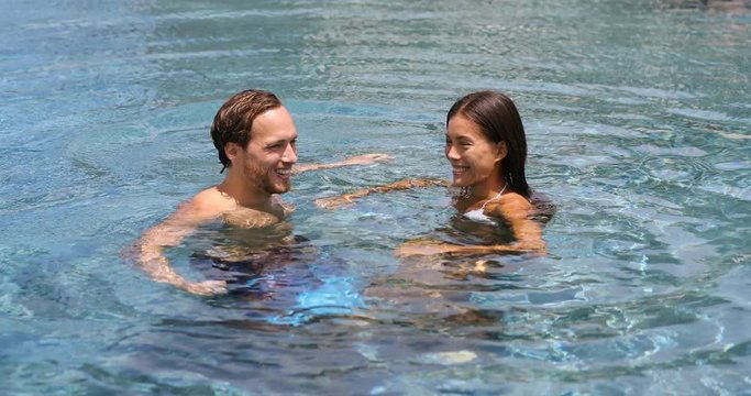 Honeymoon couple relaxing together in an infinity swimming pool in luxury resort spa retreat beach destination. Luxurious hotel travel vacation. People relaxed enjoying summer holidays. 59.94 FPS.