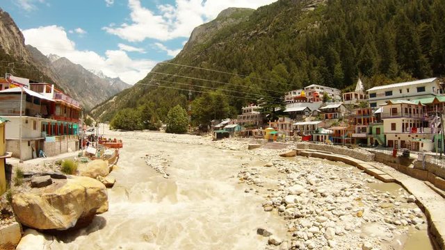 Holy river Ganges flows throgh mountain town Gangotri mountainsides with forest far peaks blues sky with white clouds