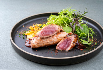 Traditionell gebratenes Spanferkel Filet mit Bratkartoffel und Salat angeboten als closeup in einem Modern Design Teller mit scharfer Sauce