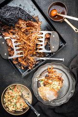 Traditional barbecue pulled pork piece of Bosten butt torn to bits with coleslaw and burger as top view on a board