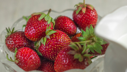 Glass bowl full of fresh strawberries on a table. Front view. Health breakfast or snack concept.