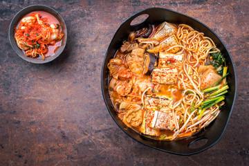 Traditional Korean kimchi jjigae with grilled pork belly and ramen as top view in a modern design Japanese cast-iron roasting dish