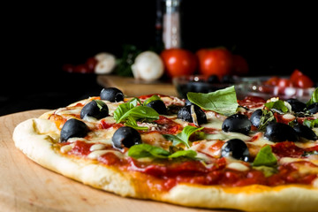 Baked pizza with salami pepperoni, black olives, basil and mozarella cheese.