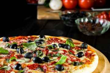 Baked pizza with salami pepperoni, black olives, basil and mozarella cheese.