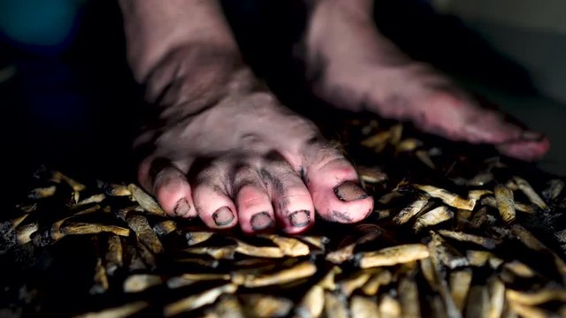 Dirty grungy homeless looking man's feet standing on spent hand rolled cigarettes in darkness.