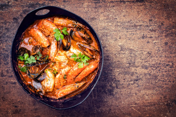 Traditional Catalan fish stew romesco de peix with prawns, mussels and fish as top view in a modern...