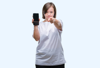 Young adult woman with down syndrome showing smartphone screen over isolated background pointing with finger to the camera and to you, hand sign, positive and confident gesture from the front