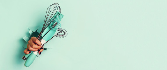 Woman hand holding kitchen utensils on blue background. Baking tools - brush, whisk, spatula. Bakery, cooking, healthy homemade food concept. Copy space