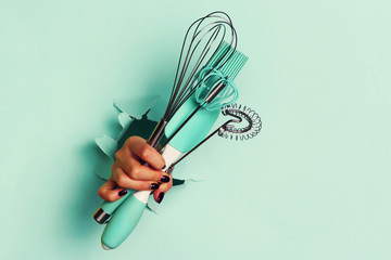 Woman hand holding kitchen utensils on blue background. Baking tools - brush, whisk, spatula. Bakery, cooking, healthy homemade food concept. Copy space