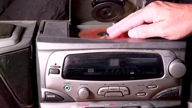 Opening an old dusty CD player then placing a CD into it and closing the lid.