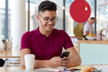 Satisfied freelancer works online, holds cellular, sends text message in social networks, sits in restaurant. Student exchanges notifications with groupmate, prepares for seminar, writes down notes