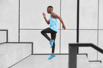 Horizontal view of male athlete dressed in activewear, has cardio running up stairs prepares for...