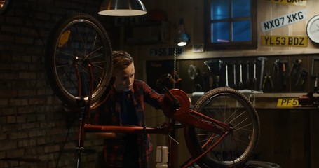 Teen boy in the garage is looking on the Internet using a tablet instruction or tutorial how to repair a bike in evening