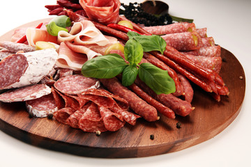 Food tray with delicious salami, pieces of sliced prosciutto crudo, sausage and basil. Meat platter with selection