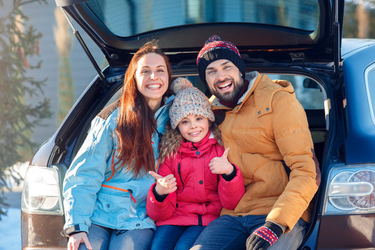 Winter vacation. Family time together outdoors standing sitting at car trunk laughing playful gitl showing thumb up close-up