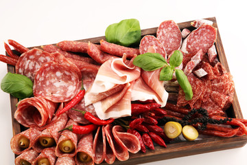 Food tray with delicious salami, pieces of sliced prosciutto crudo, sausage and basil. Meat platter...