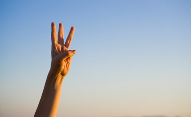 Hand doing / showing number three gesture symbol on blue summer sky nature background. Gesturing...