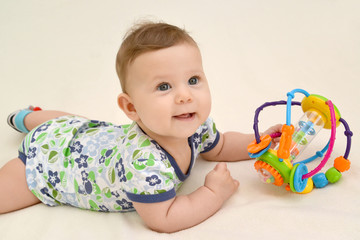 The six-months girl holds a toy lying on a stomach