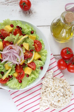 Fresh salad with lettuce, mango, tomato, onion, sesame and pomegranate. Diet food. Top view. Vegetarian and vegan food.