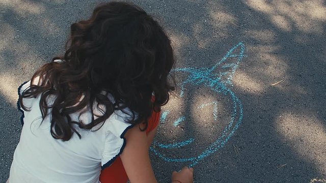 A child girl draws an unicorn on the asphalt. A little girl draws chalk in the park. 4k