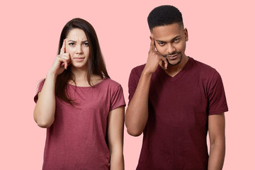 Serious mixed race woman and man keep fore fingers on temple, try to find solution in mind, wear...