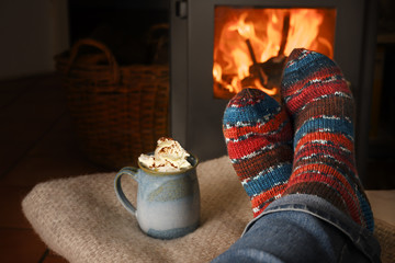feet in handmade wool socks at the fireplace and a cup of hot drink, relaxation at christmas time,...