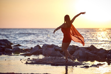 Fototapeta na wymiar girl gymnast in red dress dancing on the beach at sunrise