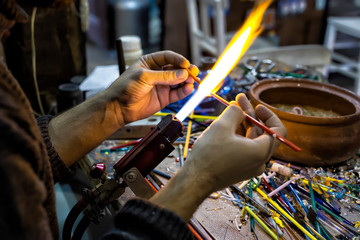 a glassblower man made Handicraft from melted glass in glassblowing workshop. Glass art is shaping at the end of glassblowing pipe.  