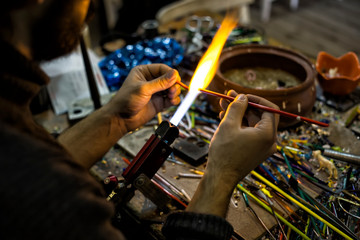 a glassblower man made Handicraft from melted glass in glassblowing workshop. Glass art is shaping at the end of glassblowing pipe.  
