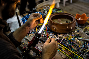 a glassblower man made Handicraft from melted glass in glassblowing workshop. Glass art is shaping at the end of glassblowing pipe.  