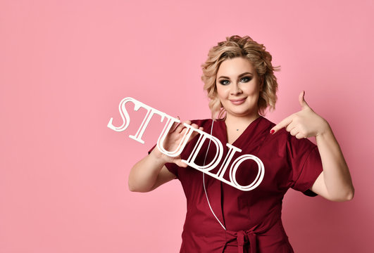 Woman hold studio wooden sign and pointing finger on light pink 