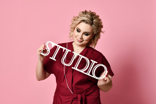 Woman hold studio wooden sign and looking down on light pink