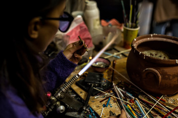 a glassblower women made Handicraft from melted glass in glassblowing workshop. Glass art is shaping at the end of glassblowing pipe.  