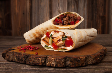 Burrito and shawarma wraps with beef and pork vegetables on wooden table. Copy space for text.