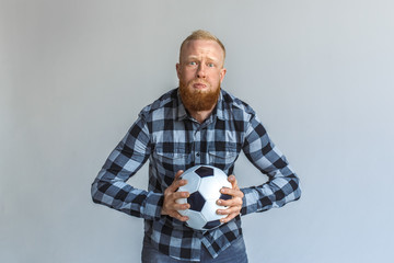 Freestyle. Mature man standing isolated on grey with ball holding breath diligently