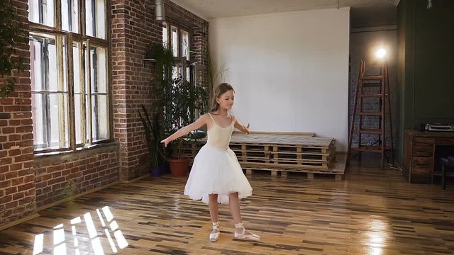 Young graceful ballerina in white tutu perform classical dance in the dance-hall. Beautiful slim ballerina in white dress performs ballet dance in the Studio
