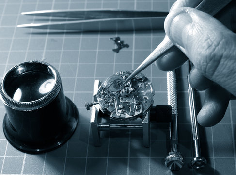 close up of watchmaker working repairing a watch, taking small piece with tweezers
