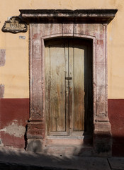 Fototapeta na wymiar Rustic old wooden doorway set against a colorful painted wall in San Miguel de Allende, Mexico