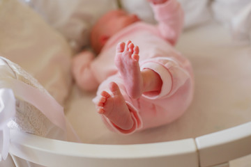 A newborn baby is lying in a white round bed, on a white sheet, with white cushion ribs. The child raised his bare feet and spread his fingers.