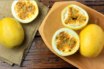 yellow passion fruit and passion fruit cut in half in wooden bowl on wooden table.
