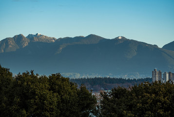 View of Vancouver downtown and north shore mountains with snow cap from high ground on a sunny day